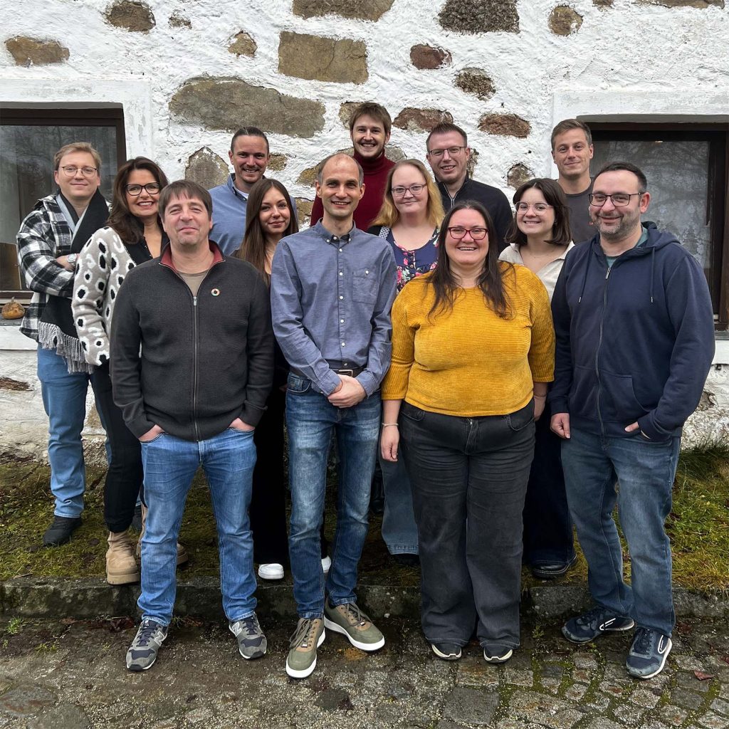Das LotzApp-Team steht gemeinsam vor einer weiß gekalkten Steinmauer