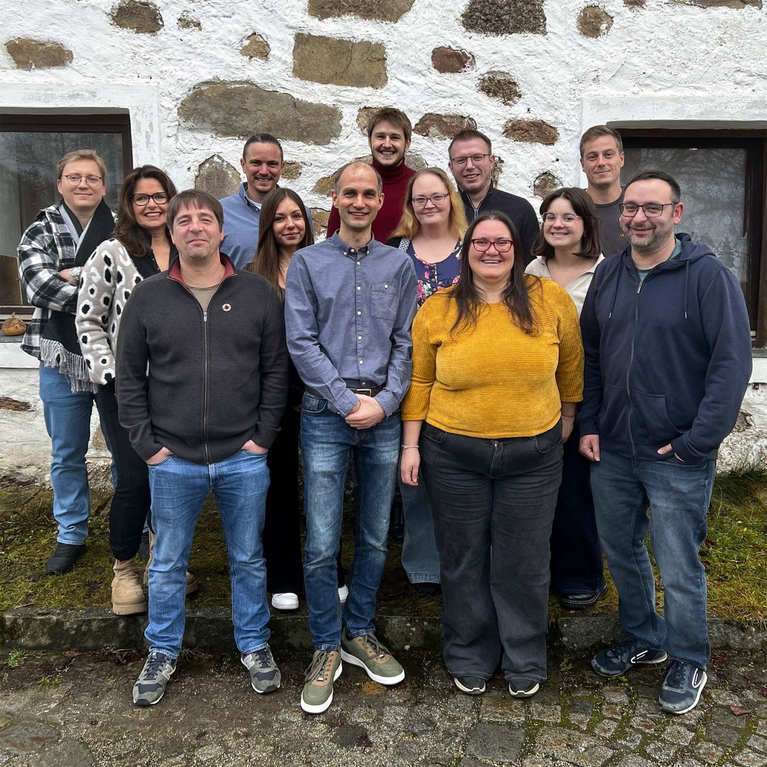 Das LotzApp-Team steht gemeinsam vor einer weiß gekalkten Steinmauer
